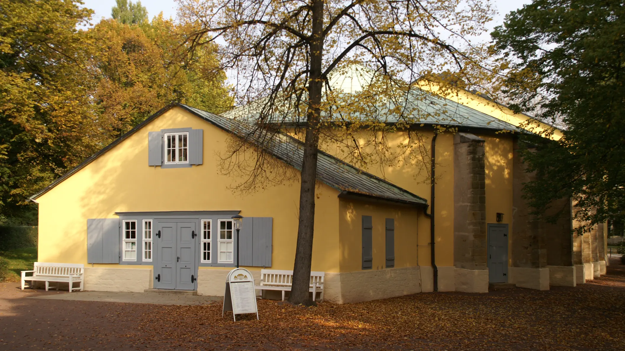 Goethe-Theater in Bad Lauchstädt im Herbst, gelbes Gebäude mit grauen Fensterläden unter Bäumen